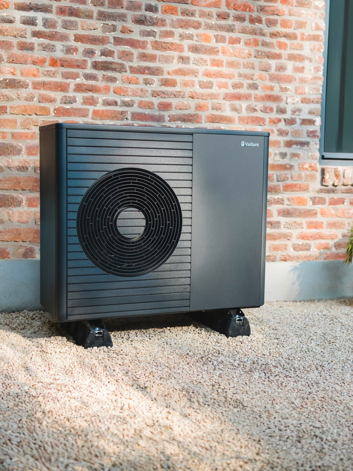 Una pompa di calore si trova davanti a un nuovo edificio, con un prato ben curato e un sentiero in primo piano.