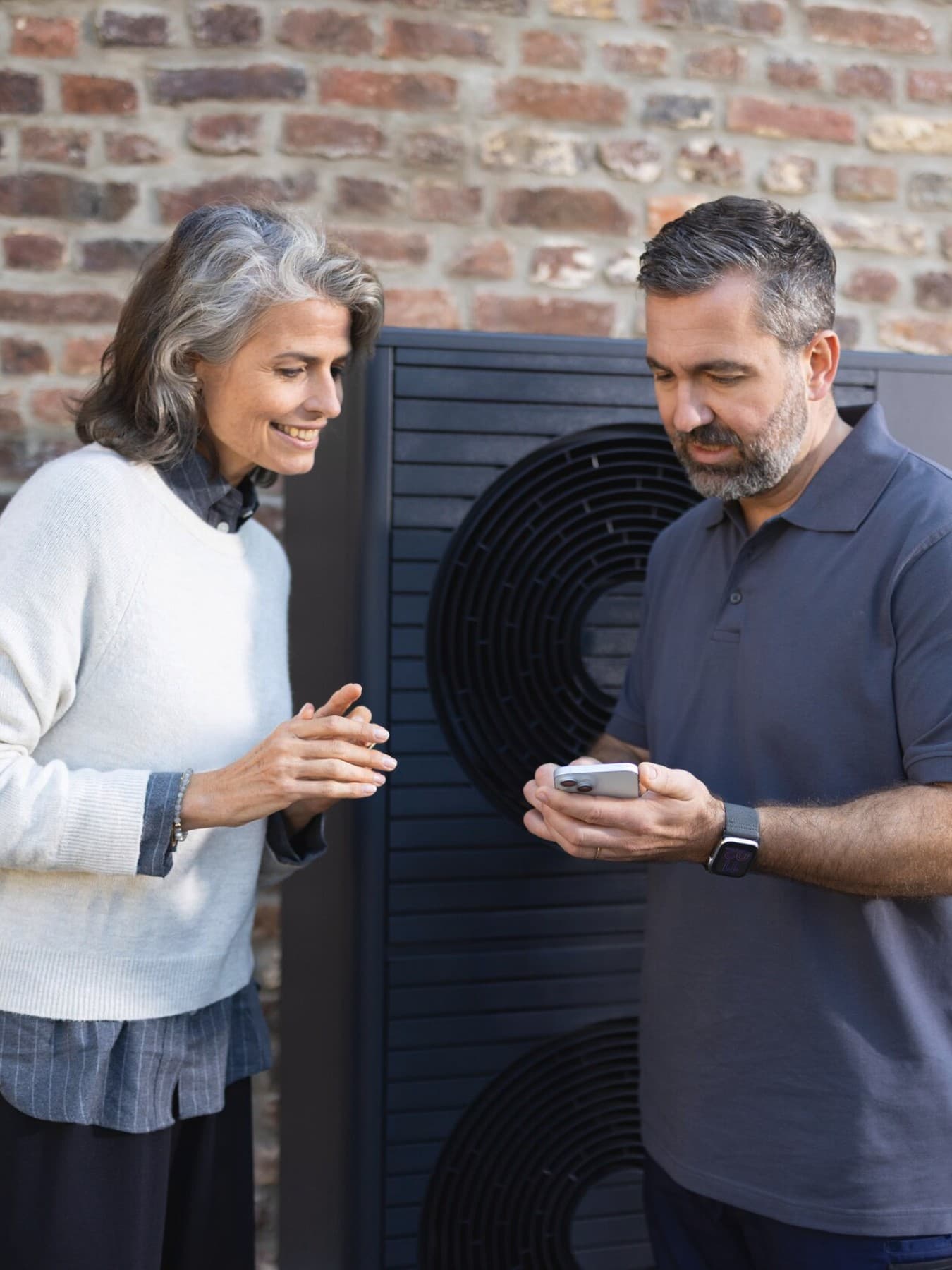 Installatore Vaillant e proprietario di casa che guardano lo smartphone davanti a una pompa di calore.