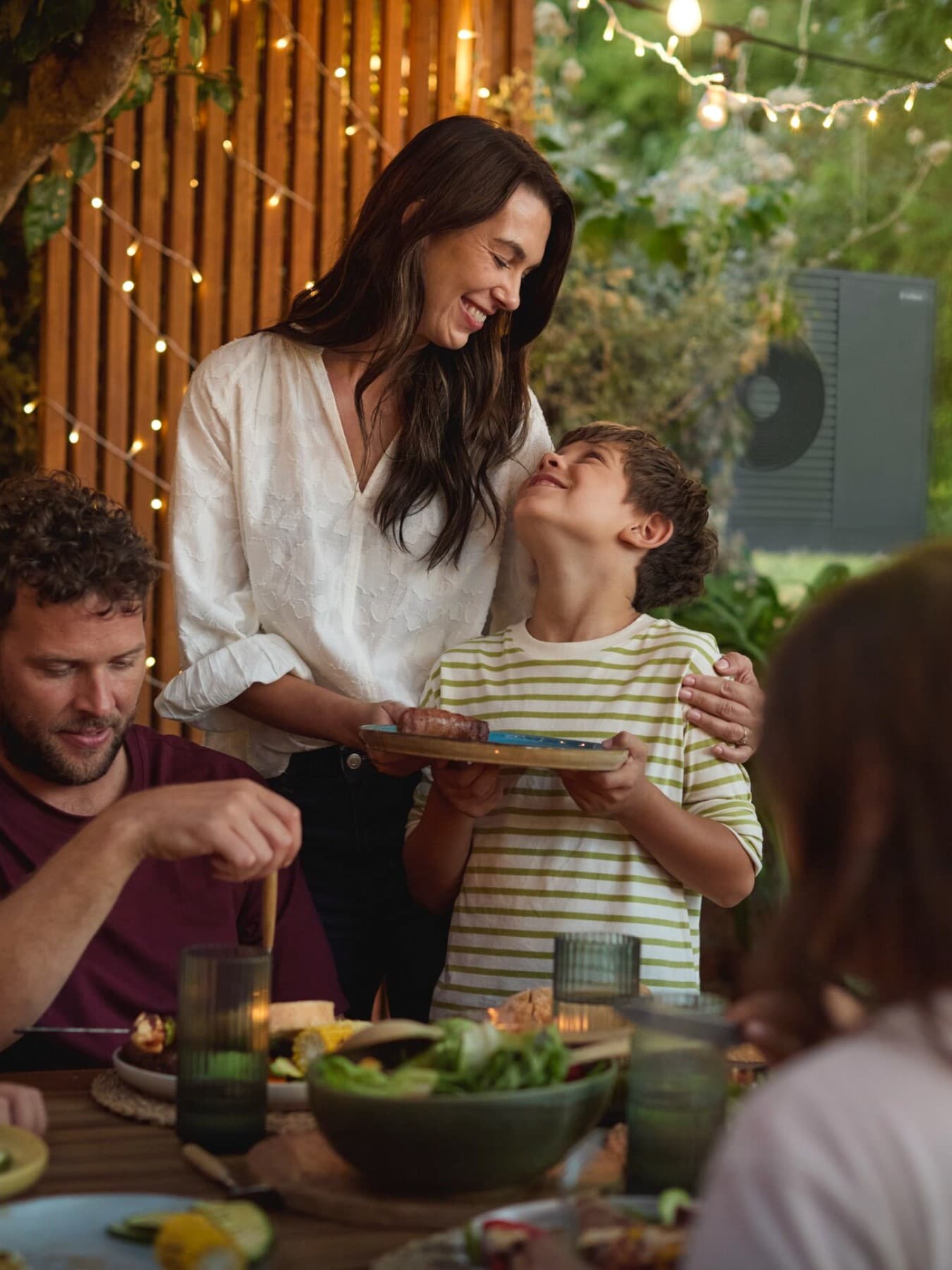 Famiglia a tavola felice con pompa di calore Vaillant sullo sfondo.