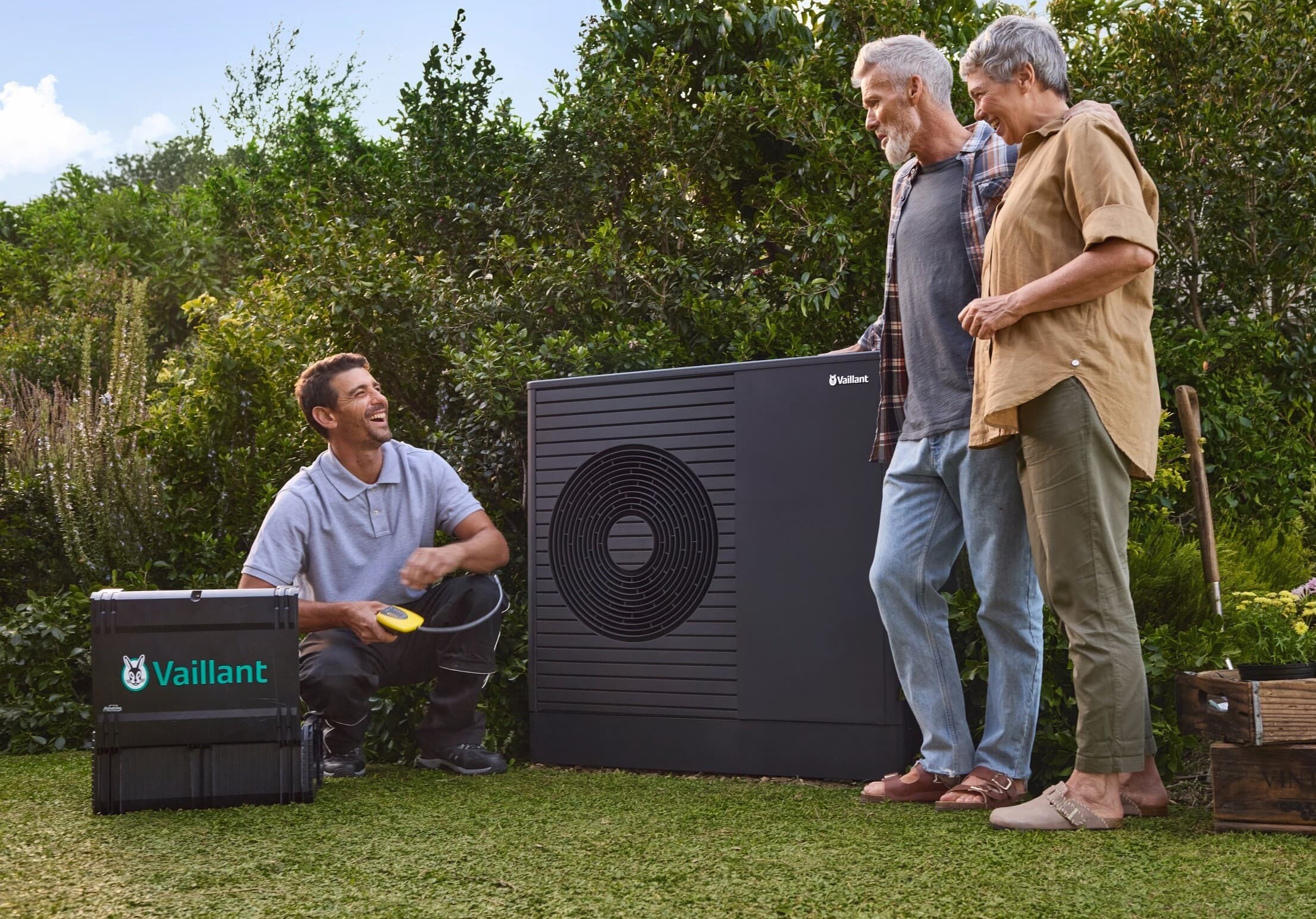 Tecnico Vaillant con due clienti in giardino mentre effettua la manutenzione di una pompa di calore.