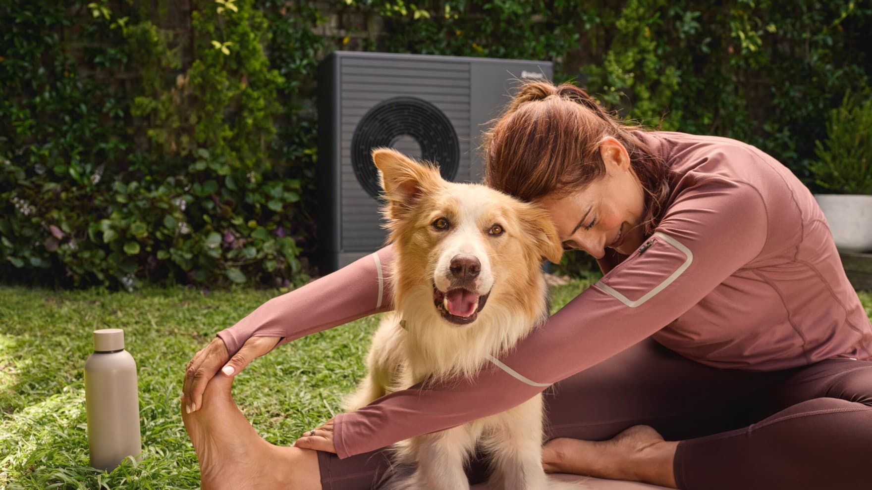 Donna con il cane in giardino. Sullo sfondo, pompa di calore Vaillant.