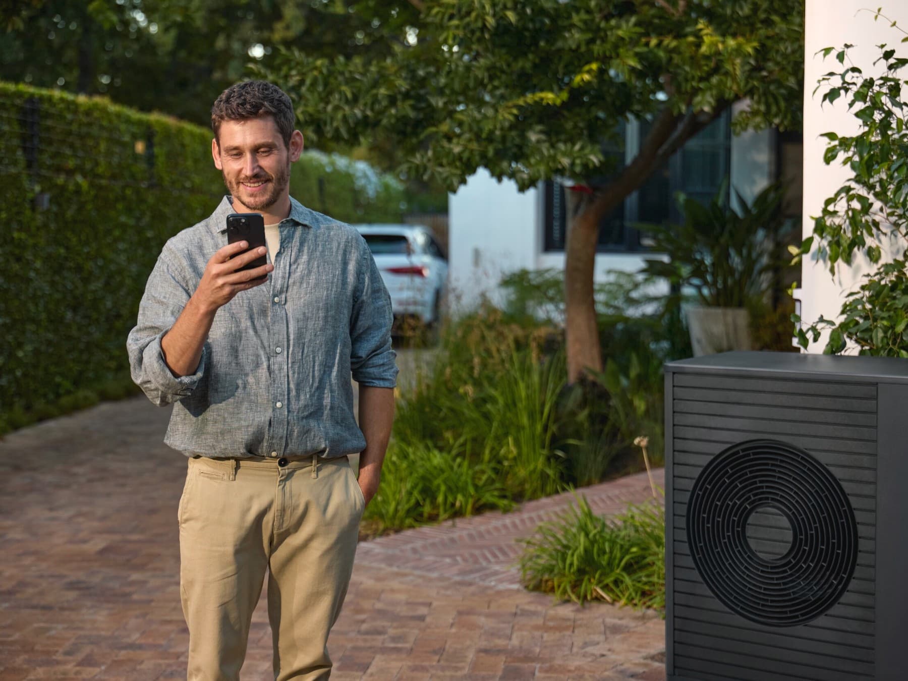 Uomo in piedi accanto a una pompa di calore che guarda uno smartphone