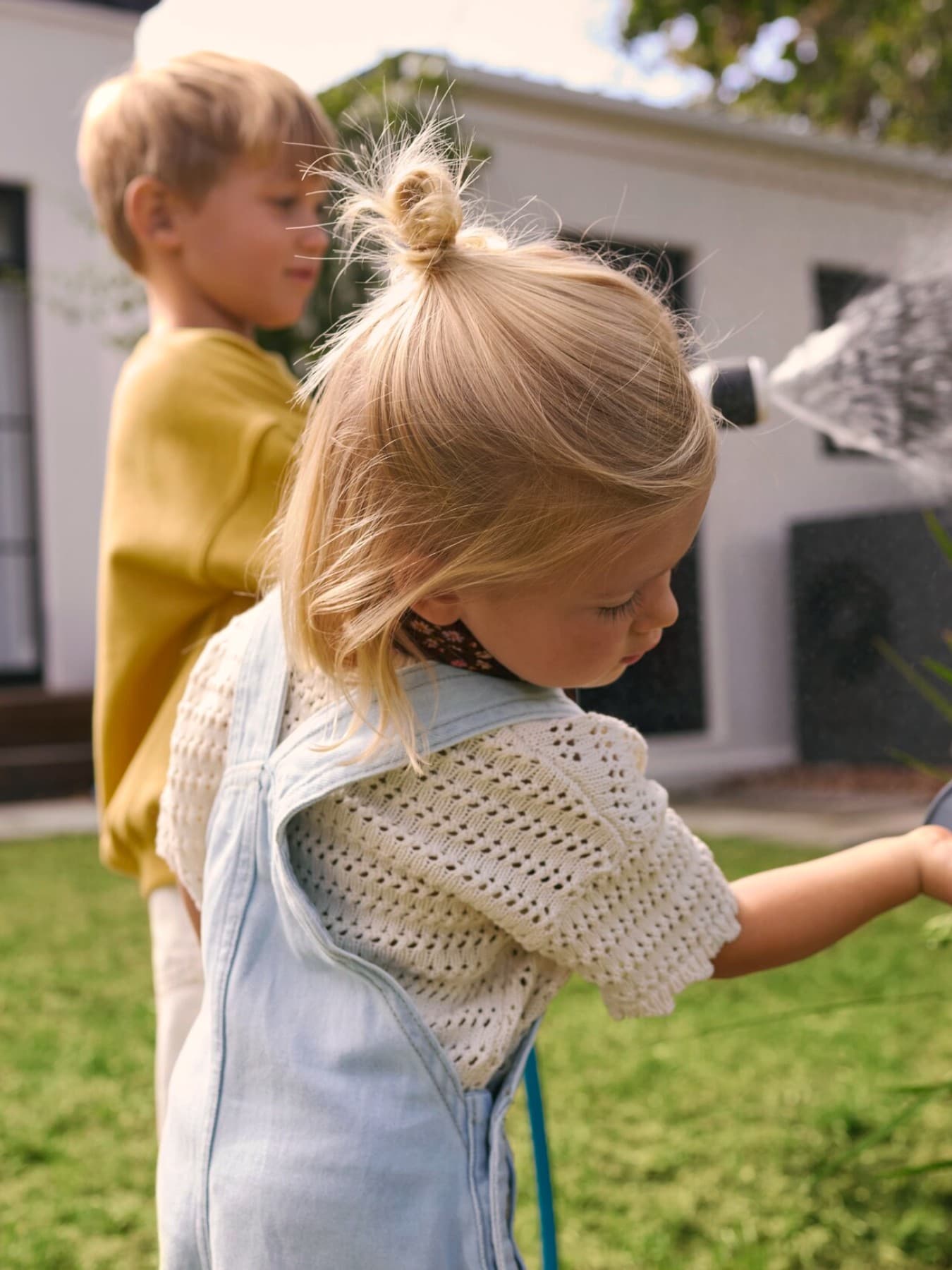 Bambini che annaffiano le piante in un giardino con una pompa di calore sullo sfondo.