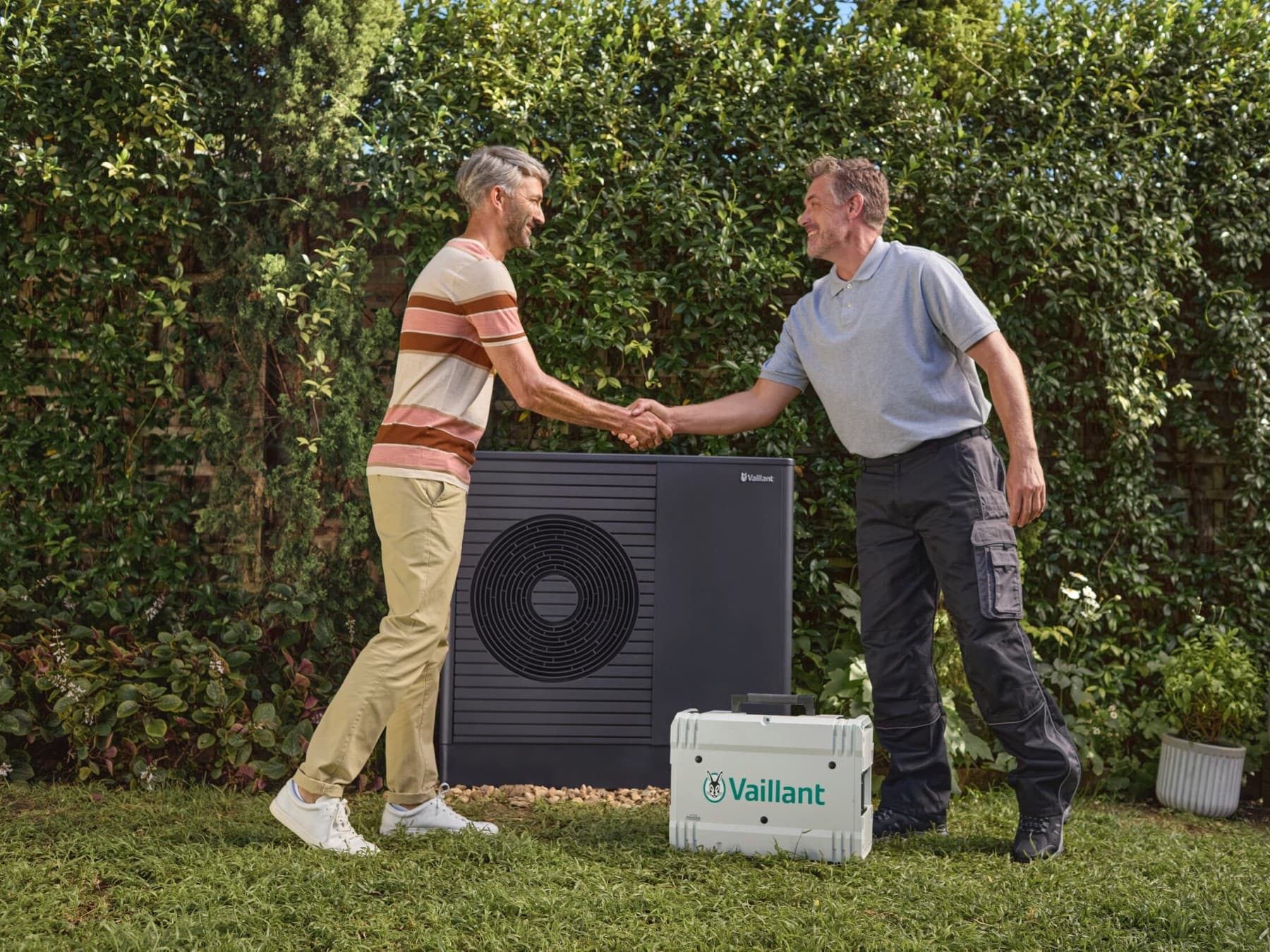 Cliente e tecnico Vaillant in giardino si stringono la mano in giardino davanti a una pompa di calore Vaillant.