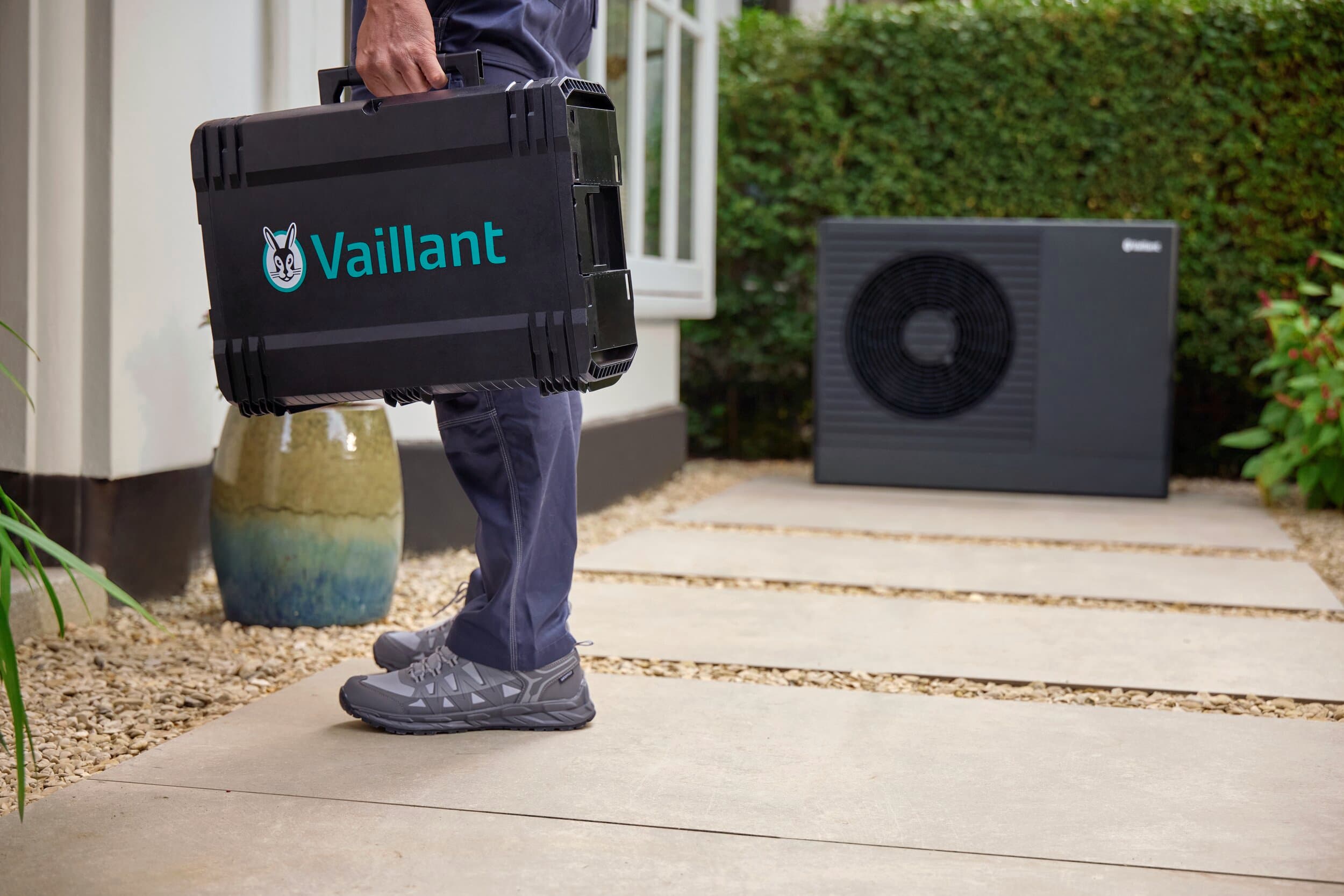 Professionista Vaillant davanti alla porta di casa di un cliente. Sullo sfondo, una pompa di calore Vaillant.