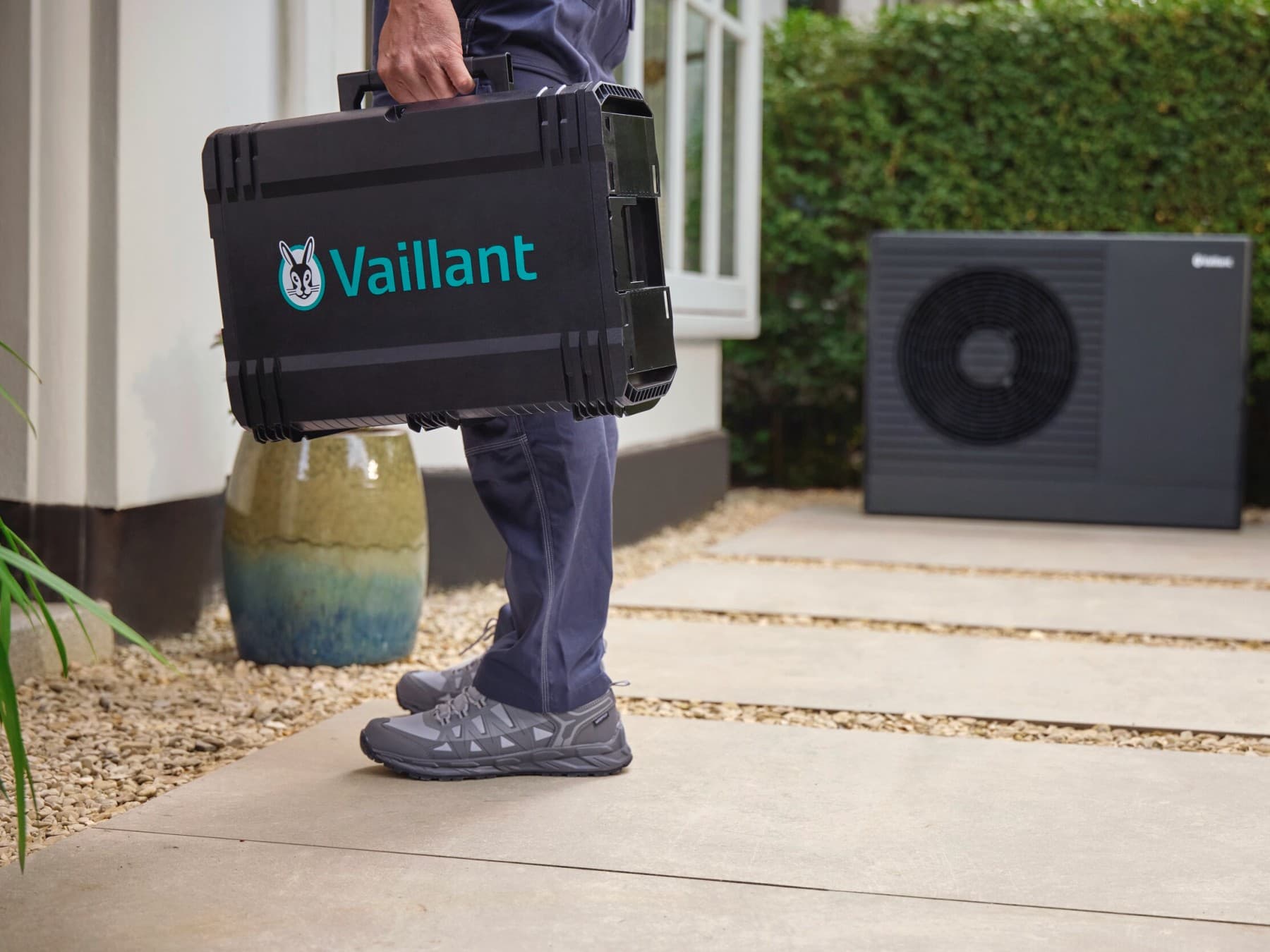 Tecnico Vaillant con valigetta attrezzatura davanti a un'unità esterna di pompa di calore in giardino