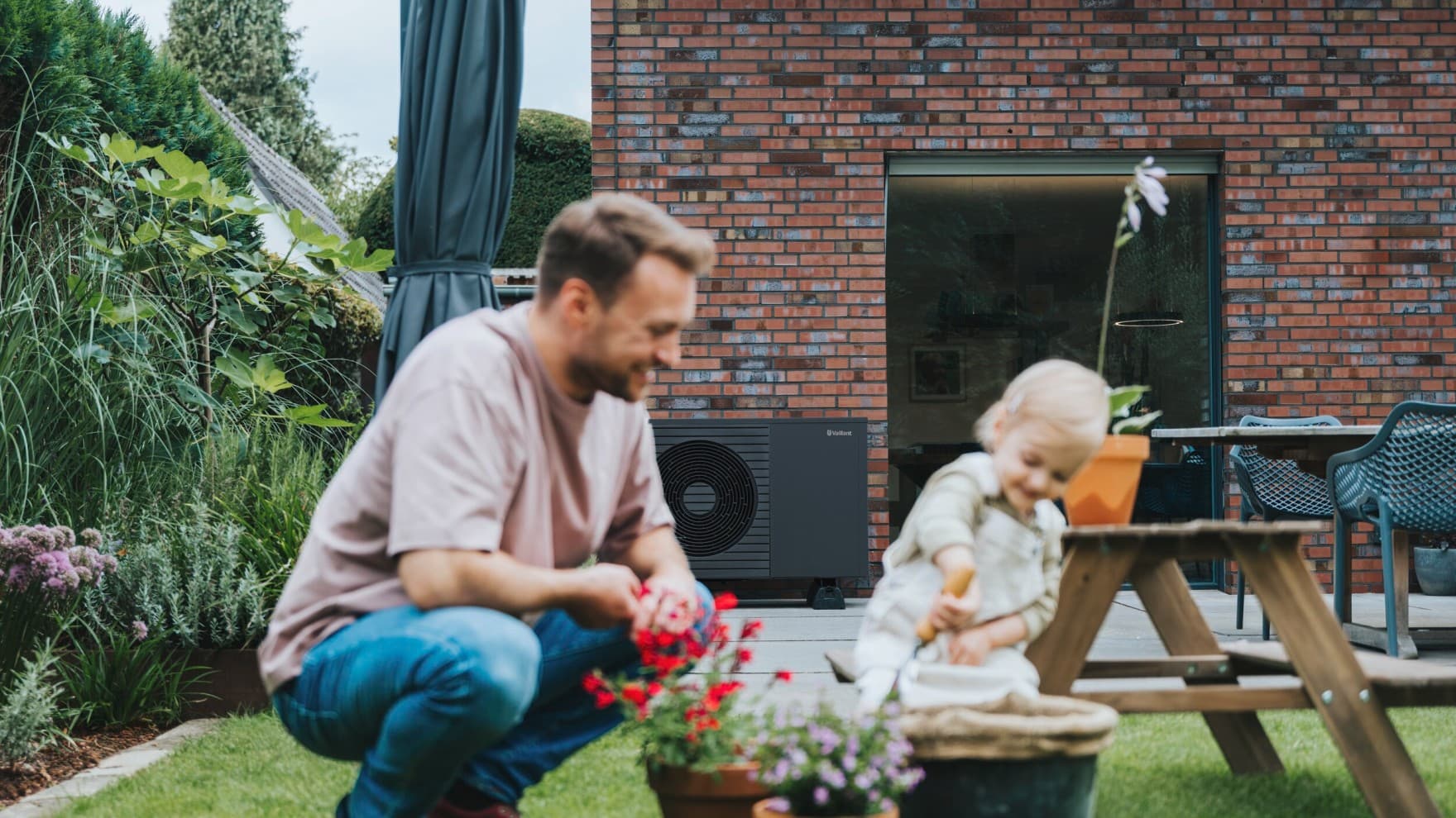 Padre e bambino che giocano in giardino con unità esterna della pompa di calore Vaillant aroTHERM pro