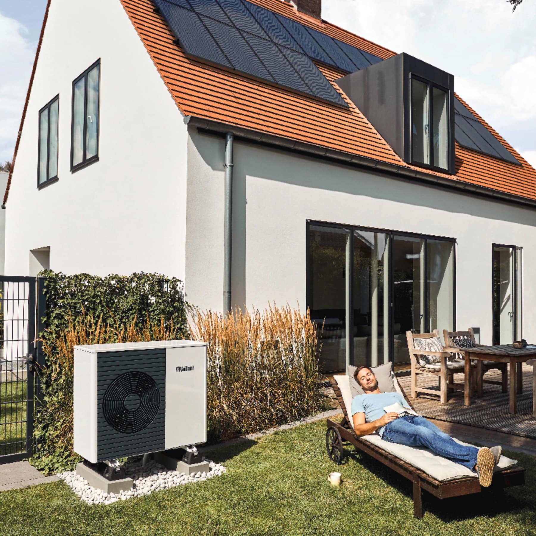 Uomo che si rilassa in giardino accanto all'unità esterna della pompa di calore Vaillant aroTHERM