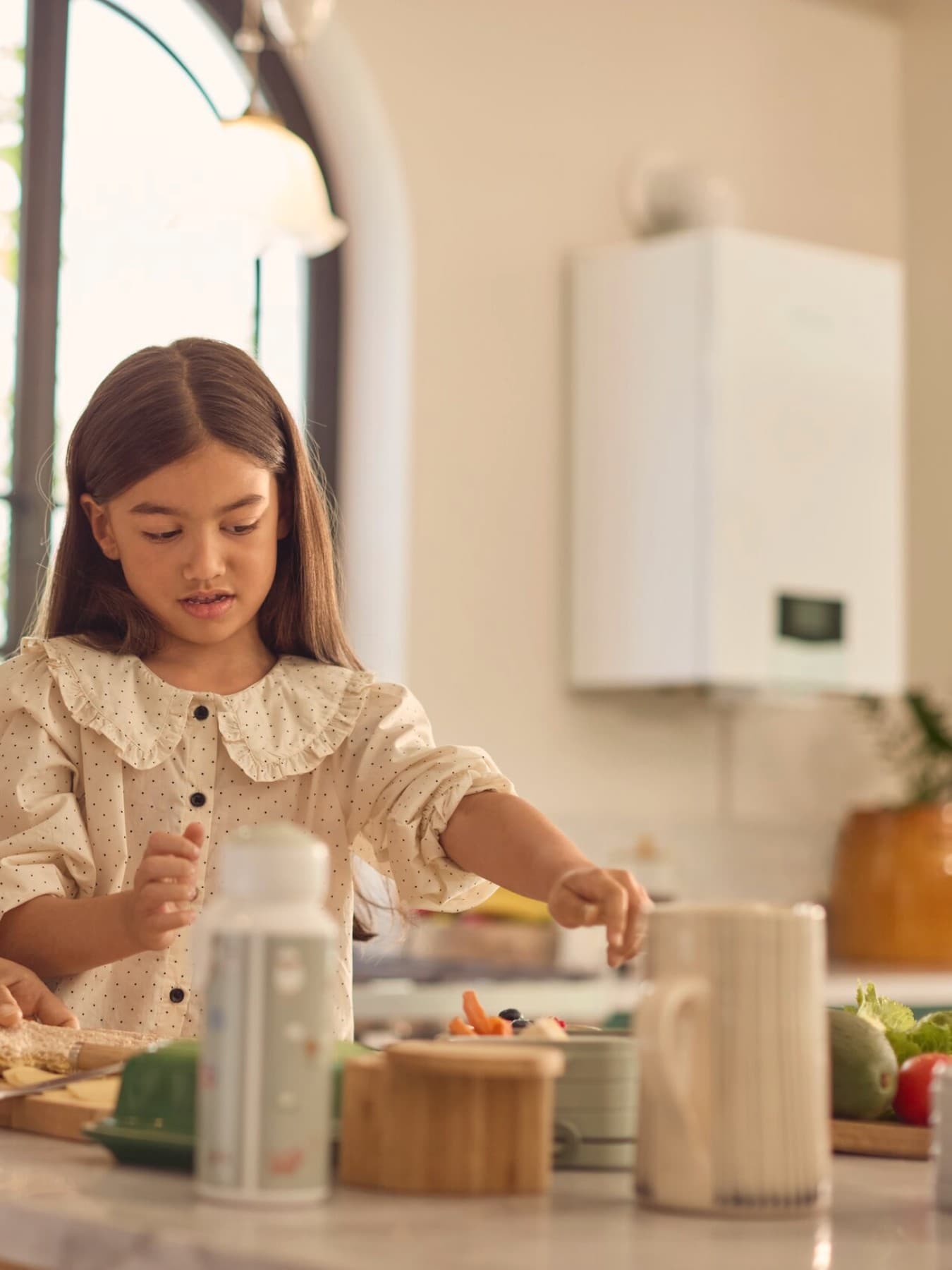 Bambina cucina con la mamma. Sullo sfondo, una caldaia ecoTEC plus Vaillant.